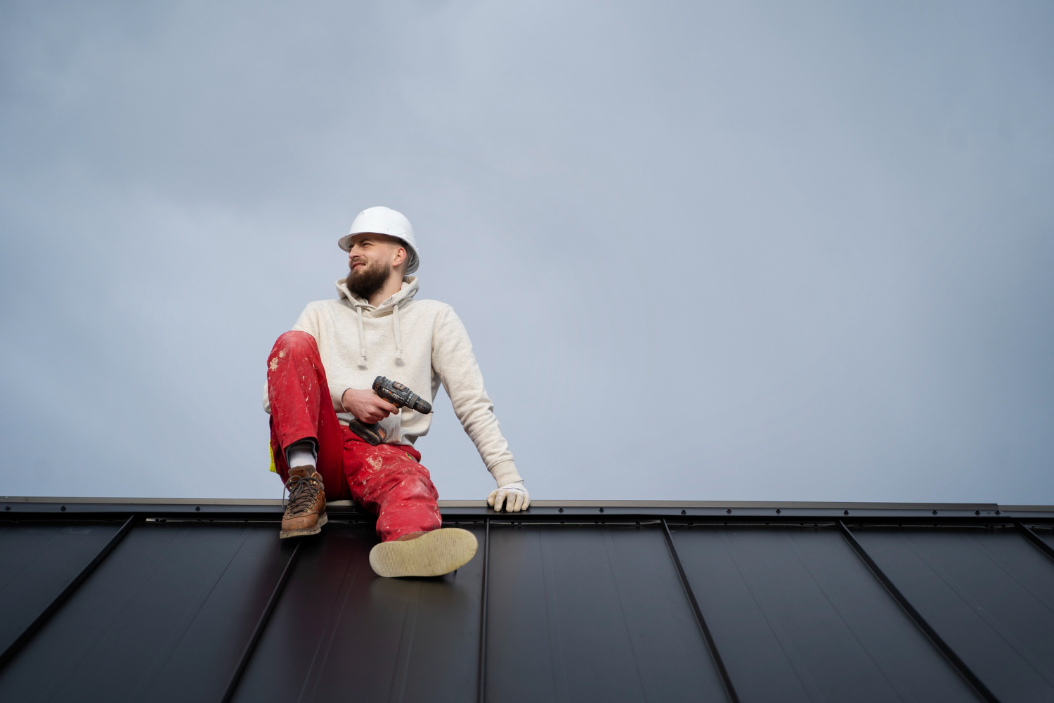 Professional roofer sitting on a metal roof prepared for elastomeric coating application.