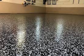 A high-gloss, gray and black decorative flake polyaspartic garage floor coating in a luxury home garage featuring a blue sports car and organized workshop.